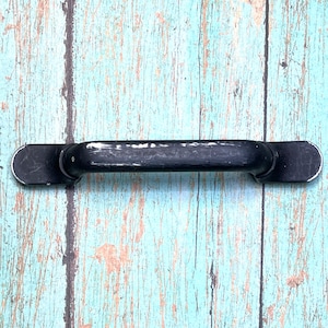 Pode incluir: Maçaneta de porta de metal preto com bordas arredondadas. A maçaneta está montada em uma superfície de madeira azul claro.