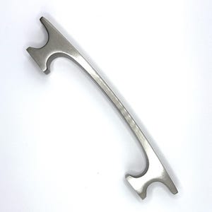 May include: A brushed nickel cabinet pull with a curved design and a rectangular shape at each end.