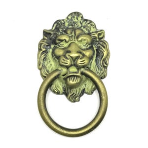 Pode incluir: Batedor de porta com cabeça de leão em latão antigo com uma alça circular. O rosto do leão é detalhado com uma juba texturizada e traços faciais. O batedor tem uma aparência envelhecida, com toques de verde e dourado.