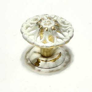 May include: White and gold decorative cabinet knob with a floral design. The knob has a round base and a raised, ornate top.