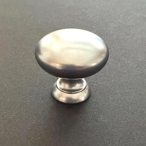 May include: A brushed nickel cabinet knob with a rounded top and a decorative base. The hardware is designed for use on drawers and cabinet doors. The knob is a neutral silver color.