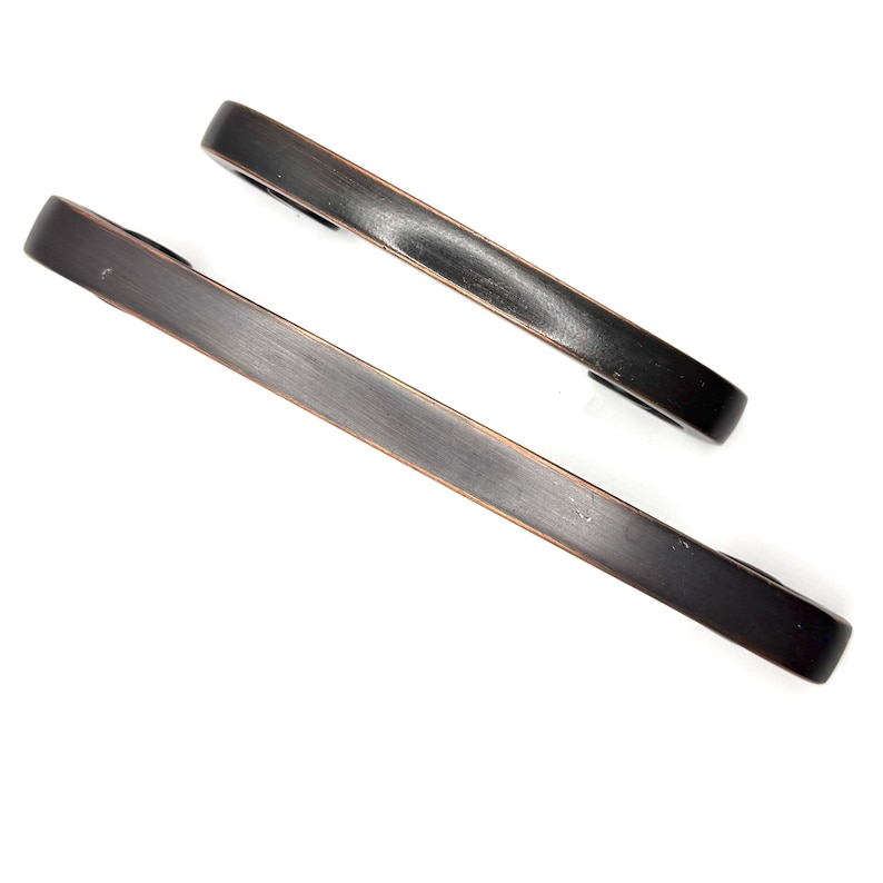 Pode incluir: Duas puxadores de arm&aacute;rio de cor bronze com acabamento em metal escovado. Os puxadores s&atilde;o retangulares com extremidades arredondadas. O hardware foi projetado para f&aacute;cil instala&ccedil;&atilde;o.