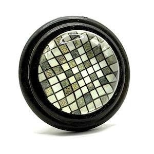 May include: A black round knob with a glass insert featuring a geometric pattern of white and gray squares.