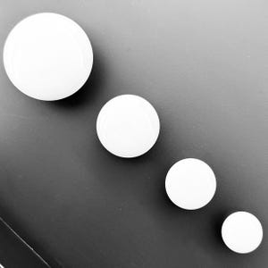 Może przedstawiać: Cztery białe, okrągłe gałki ceramiczne w różnych rozmiarach, ułożone w kolejności malejącej od lewej do prawej.