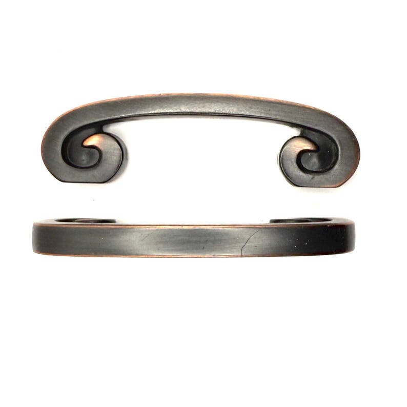 Pode incluir: Duas puxadores de arm&aacute;rio em bronze antigo. O puxador superior tem um design curvo com volutas decorativas em cada extremidade. O puxador inferior &eacute; uma barra retangular simples. Ambos os puxadores t&ecirc;m um acabamento envelhecido.