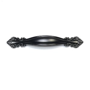 May include: Black metal cabinet pull with a decorative, ornate design. The pull has a slightly curved shape and a smooth, polished finish.