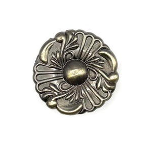 May include: Ornate, antique-style metal furniture knob with a central, rounded design and detailed floral and leaf patterns. The knob has a bronze finish and is set against a white background.