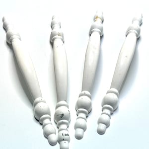 Könnte beinhalten: Vier weiße Keramik-Schrankknöpfe mit abgerundeter, leicht geschwungener Form und einem dekorativen, mehrstufigen Design. Die Knöpfe haben einen abgenutzten, antiken Look.