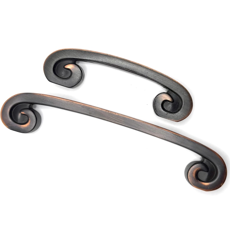 Pode incluir: Duas puxadores de arm&aacute;rio de cor bronze com um design curvo e extremidades decorativas em espiral. Os puxadores s&atilde;o colocados sobre um fundo branco, mostrando seus detalhes ornamentados e acabamento. Ideais para adicionar eleg&acirc;ncia.