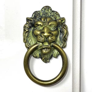 May include: A brass lion head door pull with a ring handle. The lion's face is painted in a light green colour.