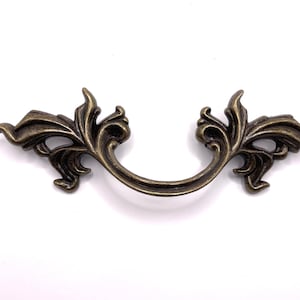 May include: A decorative antique gold-toned metal cabinet pull with a floral design.