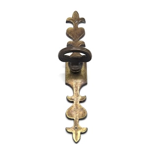 May include: An antique brass key with an ornate design. The key features a decorative handle and a long, detailed stem with heart-shaped and fleur-de-lis elements. The key is likely for a cabinet or a piece of furniture.