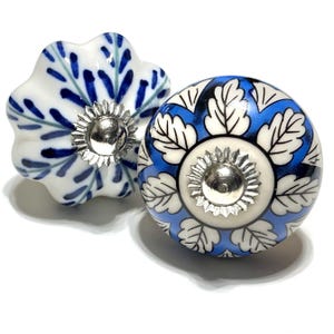 May include: Two decorative ceramic cabinet knobs. One is white with blue leaf designs, the other is round with a blue and white floral pattern. Both knobs have silver-coloured metal bases.
