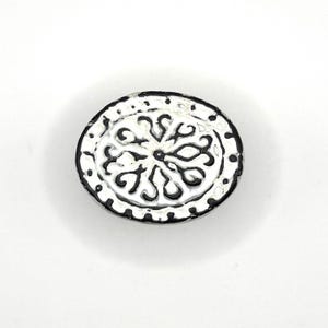 May include: White ceramic oval button with a black and white floral design.