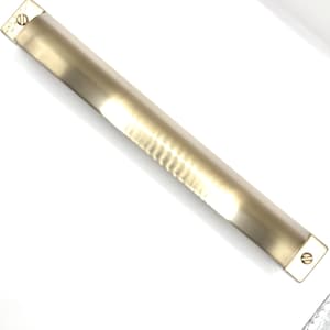 Könnte beinhalten: Ein langer, rechteckiger, messingfarbener Schrankgriff mit geriffeltem Mittelteil und abgerundeten Enden. Jedes Ende hat eine Schraube zur Befestigung. Die Hardware ist für Schubladen oder Schranktüren konzipiert.