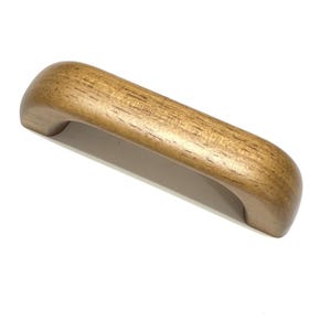 Pode incluir: Uma puxador de armário de madeira castanha clara com um design curvo. O puxador é feito de madeira e tem um padrão de grão natural. O puxador foi projetado para ser montado em uma porta ou gaveta de armário.