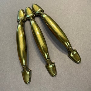 Könnte beinhalten: Drei goldfarbene Schranktürgriffe mit einer spitzen Spitze und einem dekorativen Design.