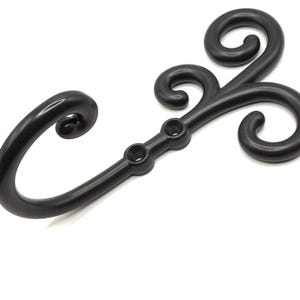Può includere: Un gancio decorativo nero con un design a volute. Il gancio presenta un braccio curvo e tre riccioli decorativi. Il gancio ha due fori per il montaggio. Il gancio è realizzato in un materiale scuro e solido.