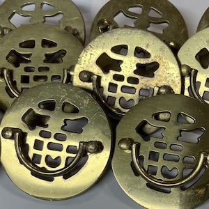 May include: A group of ten gold-toned metal cabinet knobs with a decorative, openwork design. Each knob features a circular base with a raised, stylized pattern and a curved handle.