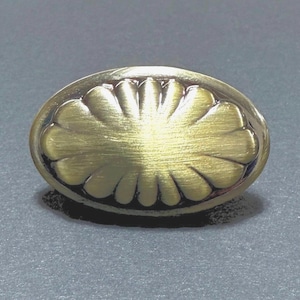 May include: Oval-shaped brass cabinet knob with a floral design. The knob has a brushed finish and a dark border, creating a contrast. The design is symmetrical and detailed, suitable for furniture hardware.