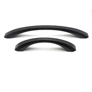 May include: Two matte black cabinet handles with a curved, arched design. The hardware features a smooth, solid finish with a consistent arc shape, presented in two different lengths to show the variation in size for furniture or cabinetry.