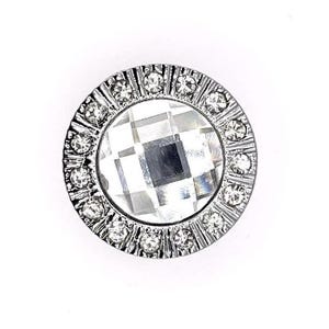 Puede incluir: Un botón redondo plateado con un strass transparente en el centro rodeado por un anillo de strass más pequeños.