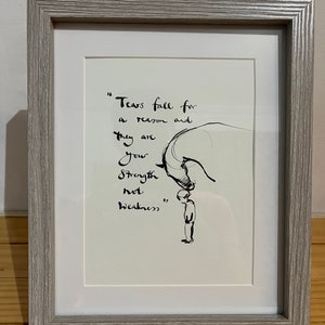 Może przedstawiać: Oprawione dzieło sztuki z szarą drewnianą ramą. Grafika przedstawia czarną ilustrację tuszem osoby i dużego zwierzęcia z cytatem "Łzy spadają z jakiegoś powodu i są twoją siłą, a nie słabością."