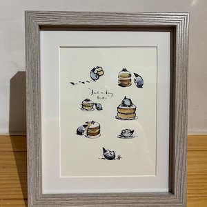 Op de afbeelding: Ingelijste illustratie met kleine, ronde wezens en pannenkoeken. Het kunstwerk zit in een lichtgrijze lijst en bevat de tekst "Just a tiny taste". De illustraties zijn in zwart-wit met enkele rode accenten.