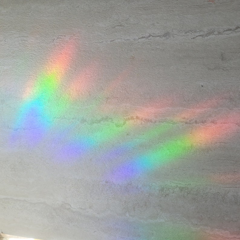 Puede incluir: Un efecto de prisma de arco&iacute;ris proyectado sobre una superficie texturizada gris claro. Los colores del arco&iacute;ris son vibrantes y se extienden en un patr&oacute;n curvo.