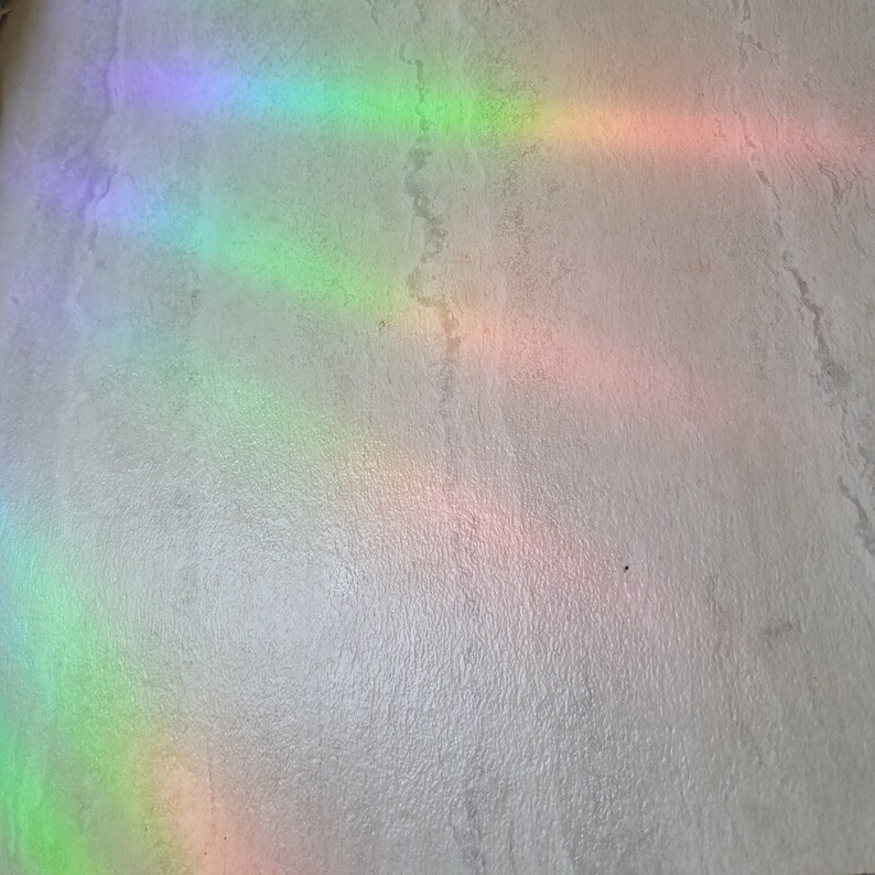 Puede incluir: Una superficie blanca texturizada con m&uacute;ltiples reflejos de luz arco&iacute;ris.