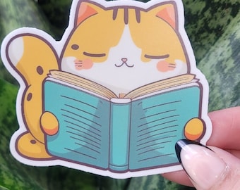 May include: A yellow and white cat with closed eyes is reading a blue book with white pages. The cat is sitting on a green plant.