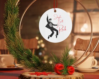 May include: A white round Christmas ornament with a black and white image of Elvis Presley in a red and white striped shirt, jumping in the air. The ornament has the text "Jingle Bell Rock" in red cursive writing.