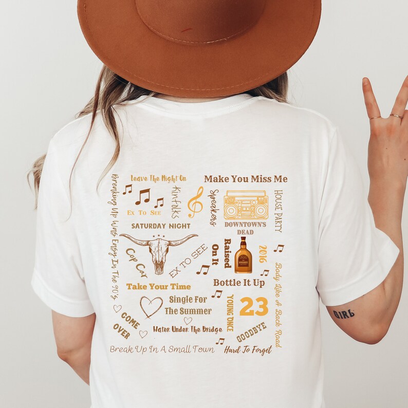 K&ouml;nnte beinhalten: Wei&szlig;es T-Shirt mit einem Design zum Thema Country-Musik. Das Design umfasst einen Stiersch&auml;del, Noten, eine Whiskyflasche und die Zahl 23. Das T-Shirt hat eine lockere Passform.
