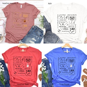 K&ouml;nnte beinhalten: Vier T-Shirts in Heather Mauve, Asch, Heather Red und True Royalblau. Jedes Shirt hat ein grafisches Design mit Text, einem Bullenkopf, Noten und der Zahl 23. Die Shirts werden auf einem Holzkleiderb&uuml;gel pr&auml;sentiert.