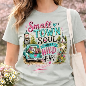 May include: A light green t-shirt with the words "Small Town Soul with a Wild Heart" in pink and teal. The graphic includes a teal truck filled with flowers, a water tower, and a church.