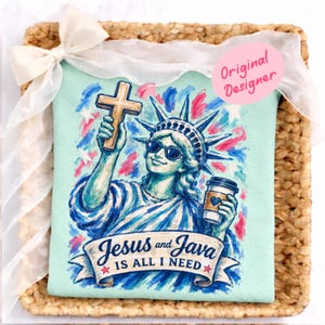 Peut inclure: T-shirt bleu clair avec un motif de la Statue de la Liberté portant des lunettes de soleil, tenant une croix et une tasse de café. Le texte "Jesus and Java is all I need" est affiché sur une bannière en dessous.