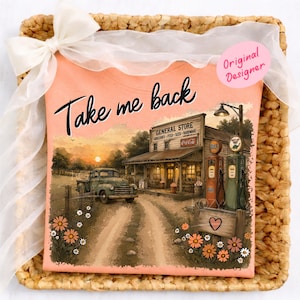 以下が含まれることがあります： 「Take me back」の文字が黒い筆記体で書かれた、桃色のTシャツ。Tシャツには、雑貨店、トラック、ガソリンスタンドのヴィンテージシーンが描かれています。白いリボンが付いた、編みかごに入っています。