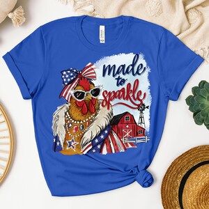 Op de afbeelding: Koningsblauw T-shirt met een cartoonkip met een zonnebril en een patriottische outfit. De afbeelding bevat de tekst "made to sparkle" en een rode schuur met een windmolen.