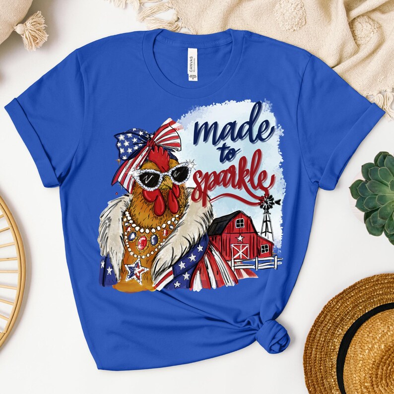 Op de afbeelding: Koningsblauw T-shirt met een cartoonkip met een zonnebril en een patriottische outfit. De afbeelding bevat de tekst "made to sparkle" en een rode schuur met een windmolen.