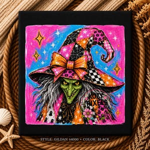 May include: A black t-shirt featuring a graphic of a green-skinned witch wearing a colorful patchwork hat with an orange bow. The design includes stars, spiderwebs, and the text KOZY PIXELS. The style is Gildan 64000, color black.