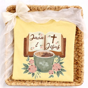 May include: Yellow t-shirt with the words "Java & Jesus" printed on it, along with a coffee cup and floral accents. The shirt is presented in a woven basket and tied with a white ribbon.