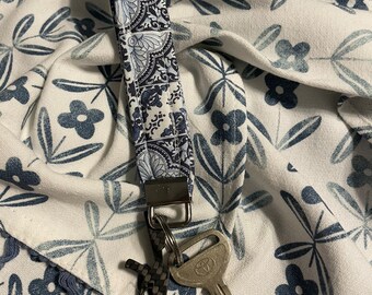 May include: A blue and white patterned fabric key chain with a silver key ring and a silver key attached.