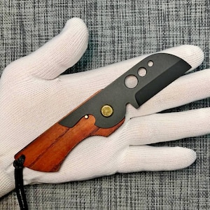 May include: A small, black pocket knife with a wooden handle. The blade has a unique design with several holes.