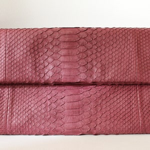 May include: A burgundy snakeskin clutch bag with a fold-over flap.
