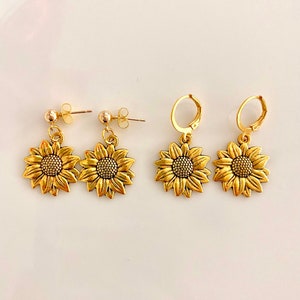 May include: A set of four gold sunflower earrings. Two earrings have a post back and two earrings have a hoop back.