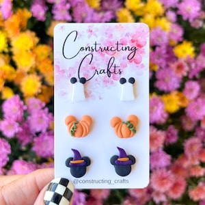 May include: A set of six Halloween-themed earrings featuring a ghost, pumpkin, and Mickey Mouse wearing a witch hat. The earrings are displayed on a white card with the text "Constructing Crafts" and the social media handle "@constructing_crafts".