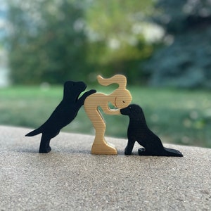 May include: Wooden figurine set of a person with two black dogs. The person is standing with their arms outstretched and the dogs are sitting on either side of them.