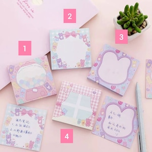 Op de afbeelding: Een set van zes pastelroze en paarse plakbriefjes met schattige cartoonberen en hartjes. De briefjes hebben verschillende ontwerpen, waaronder een snoepautomaat, een raam met gordijnen en een lege ruimte om op te schrijven.