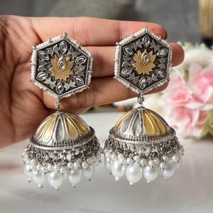 May include: A pair of silver and gold earrings with a floral design and pearl accents. The earrings are in the shape of a dome with a hexagonal top.