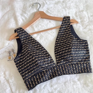 May include: A black sleeveless blouse with a deep V-neckline and gold embroidery. The embroidery features a repeating pattern of small, curved shapes.